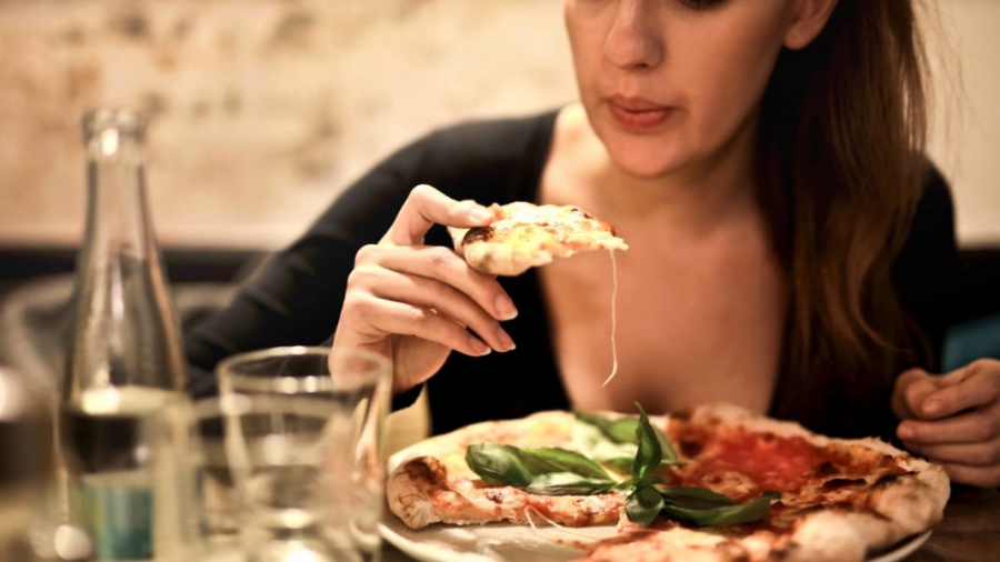 woman-holds-sliced-pizza-seats-by-table-with-glass-723031-Cropped-1-1068x601